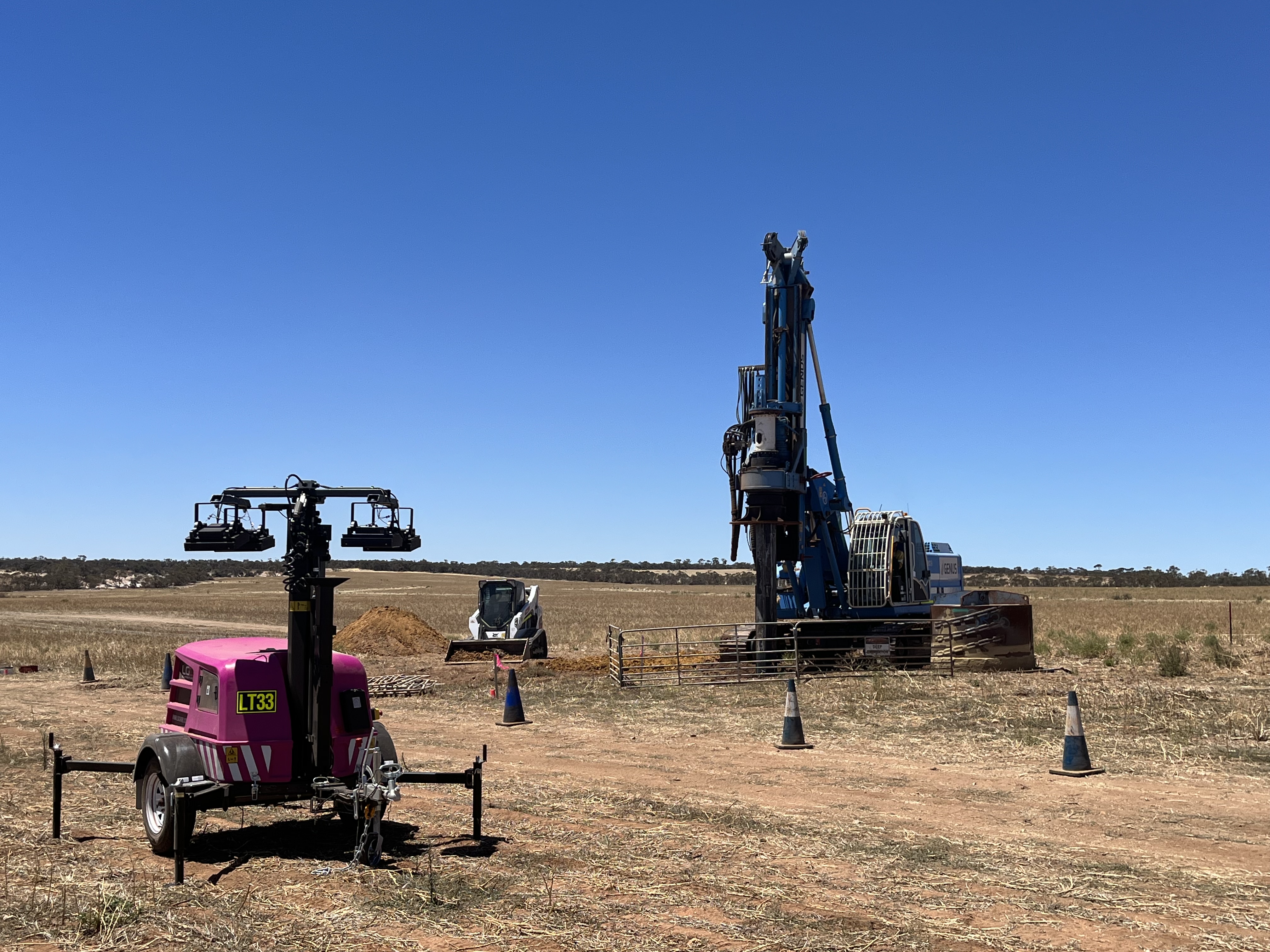 Drilling equipment and machinery set up in an open rural paddock under a clear blue sky.