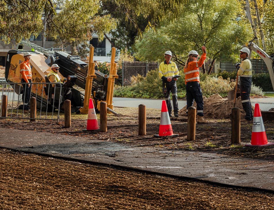 Utility workers installing underground power using trenching equipment in a coned-off work zone on a suburban street.