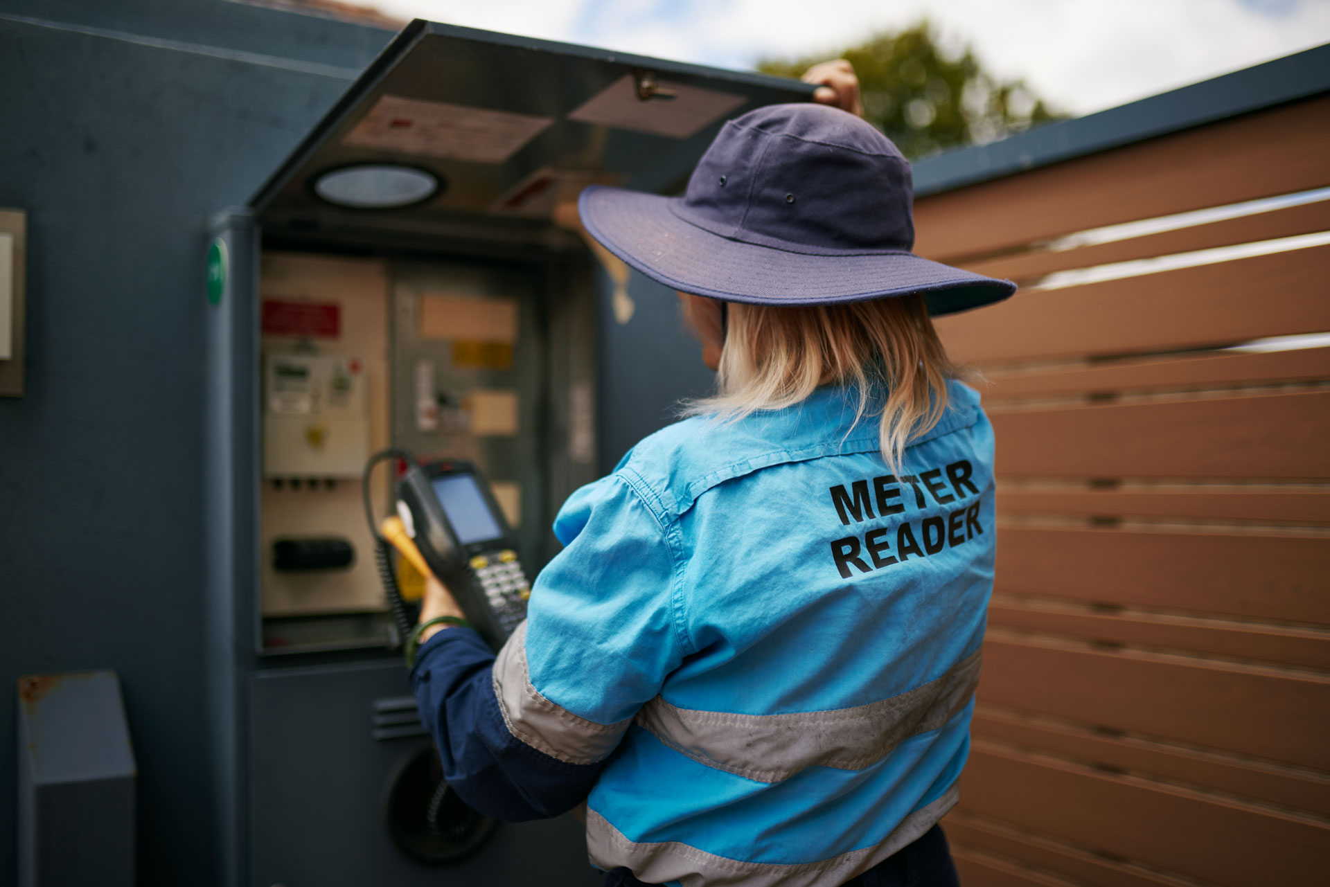 A female meter reader reading a Western Power meter on a residential property