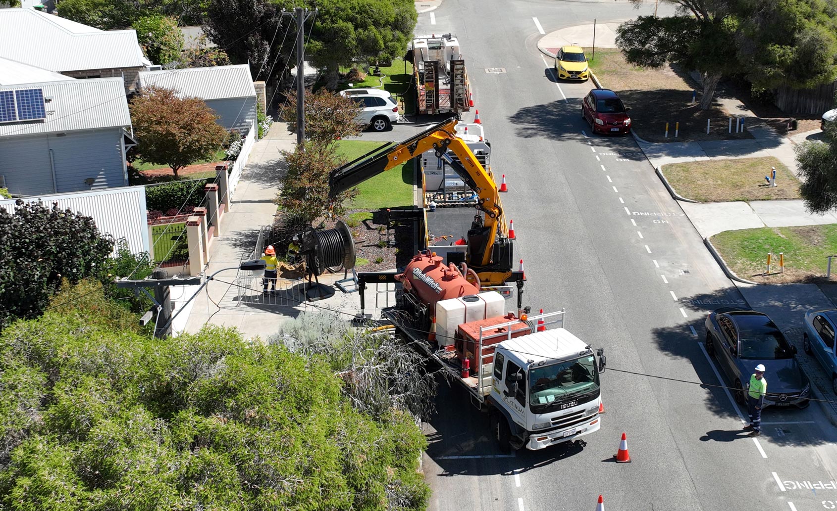 Aerial view of underground cabling being installed along a suburban street, with traffic cones and lane closures in place.