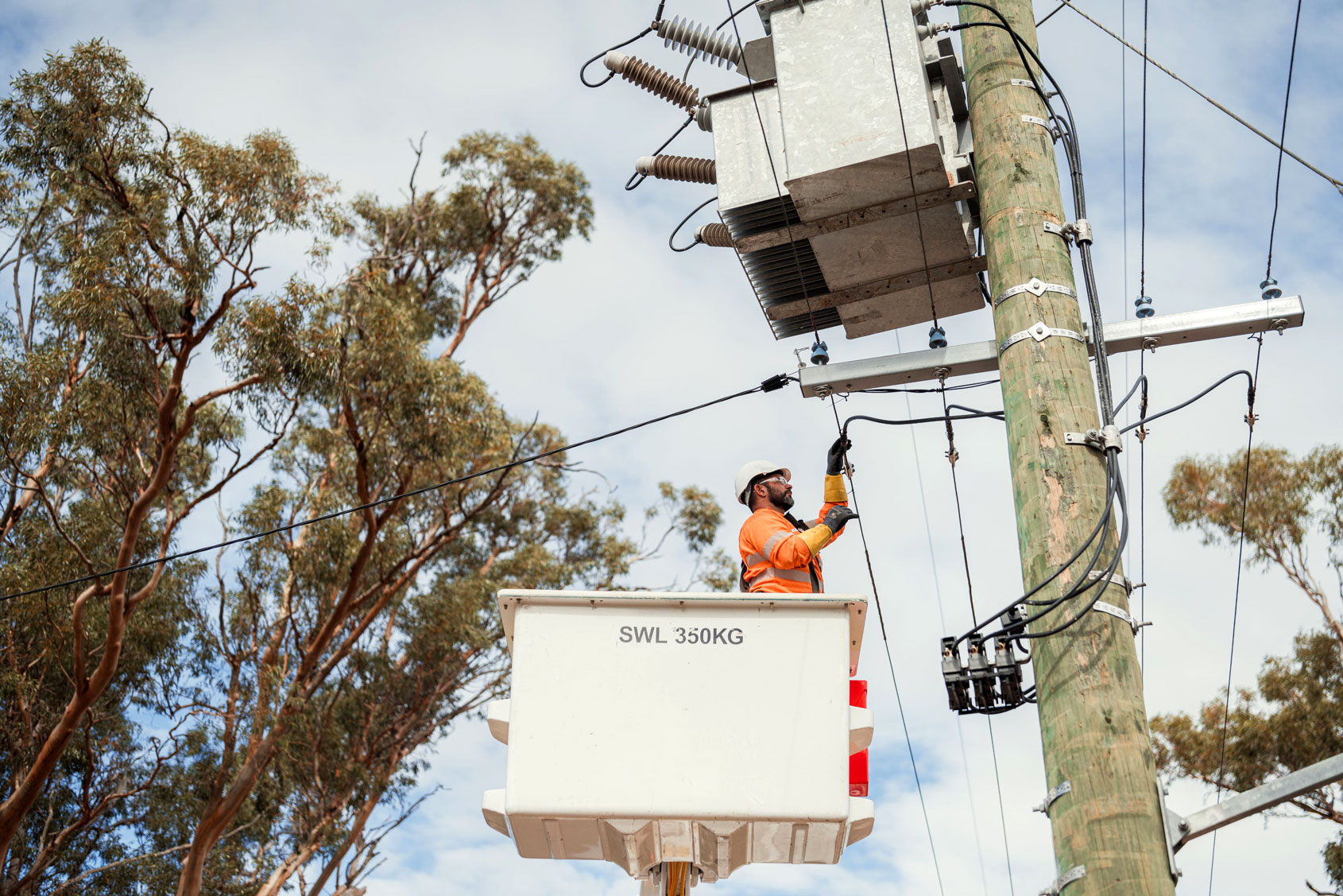 Worker in an elevated work platform performing maintenance on power lines and equipment.