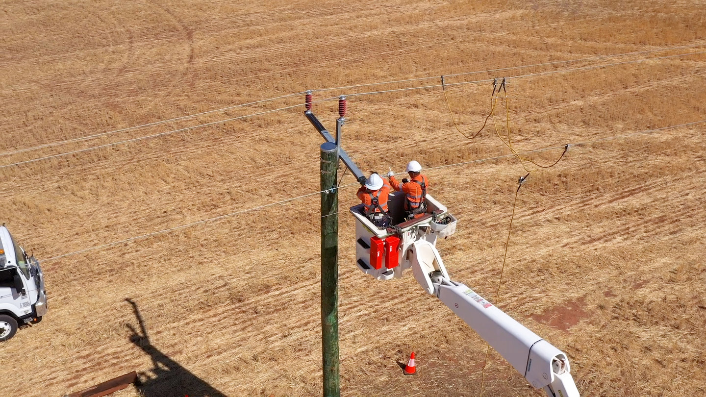 Western Power crew in a elevated work platform carrying out work on an electricity pole in a field