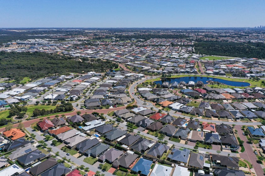 Aerial view of a dense suburban neighbourhood with roof top solar and a small winding lake.