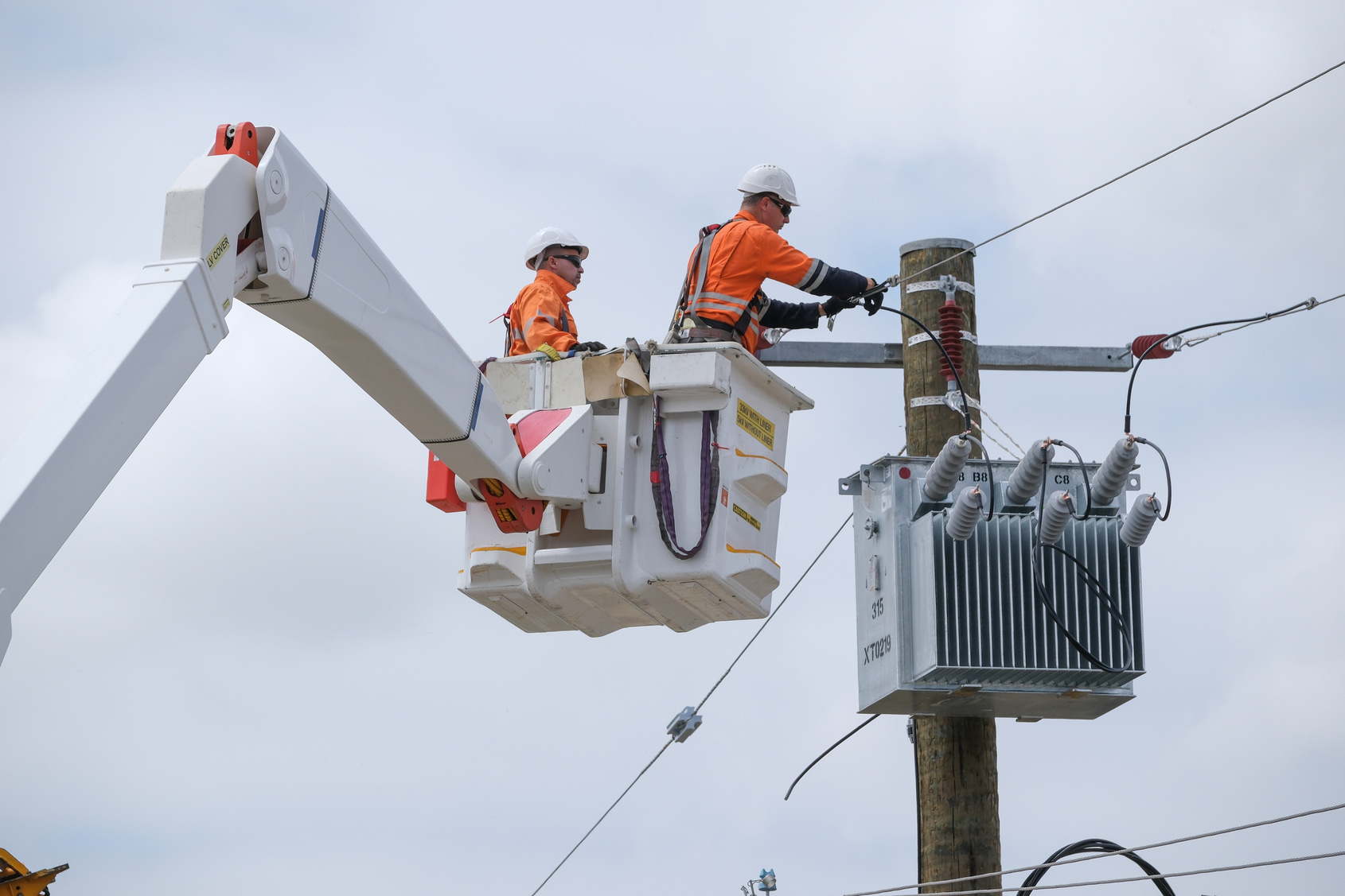 Utility workers performing maintenance on a power pole and transformer from an elevated work platform truck.