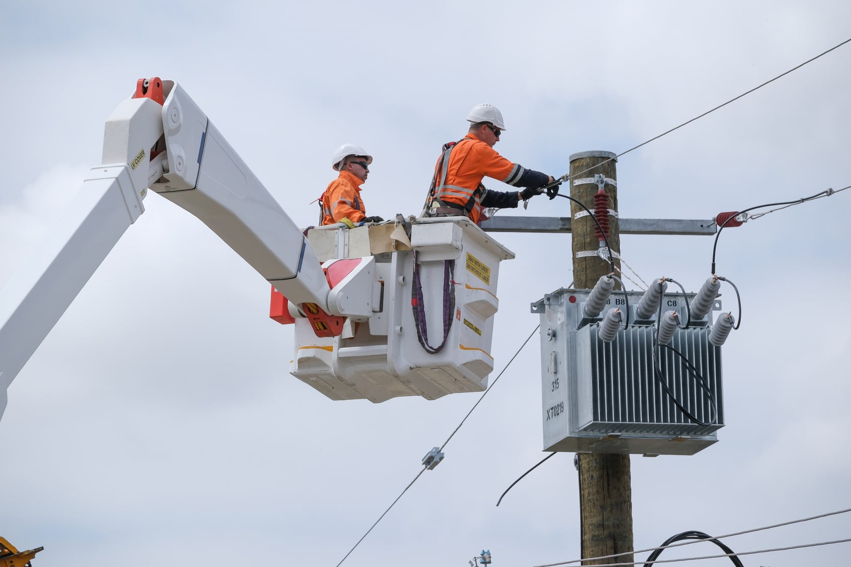 Utility workers performing maintenance on a power pole and transformer from an elevated work platform truck.