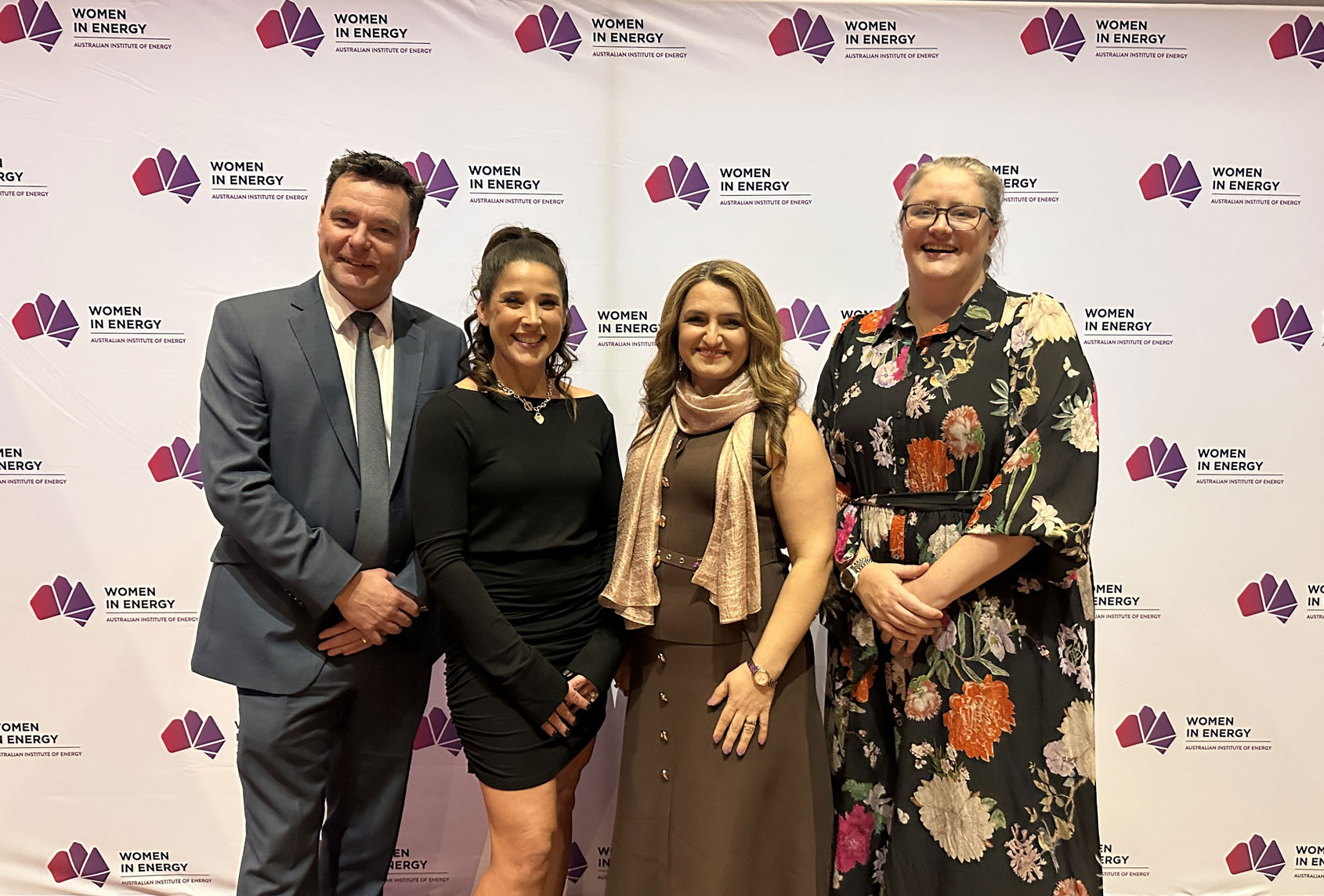 Western Power winners and acting CEO in formal attire pose in front of a Women in Energy event backdrop.