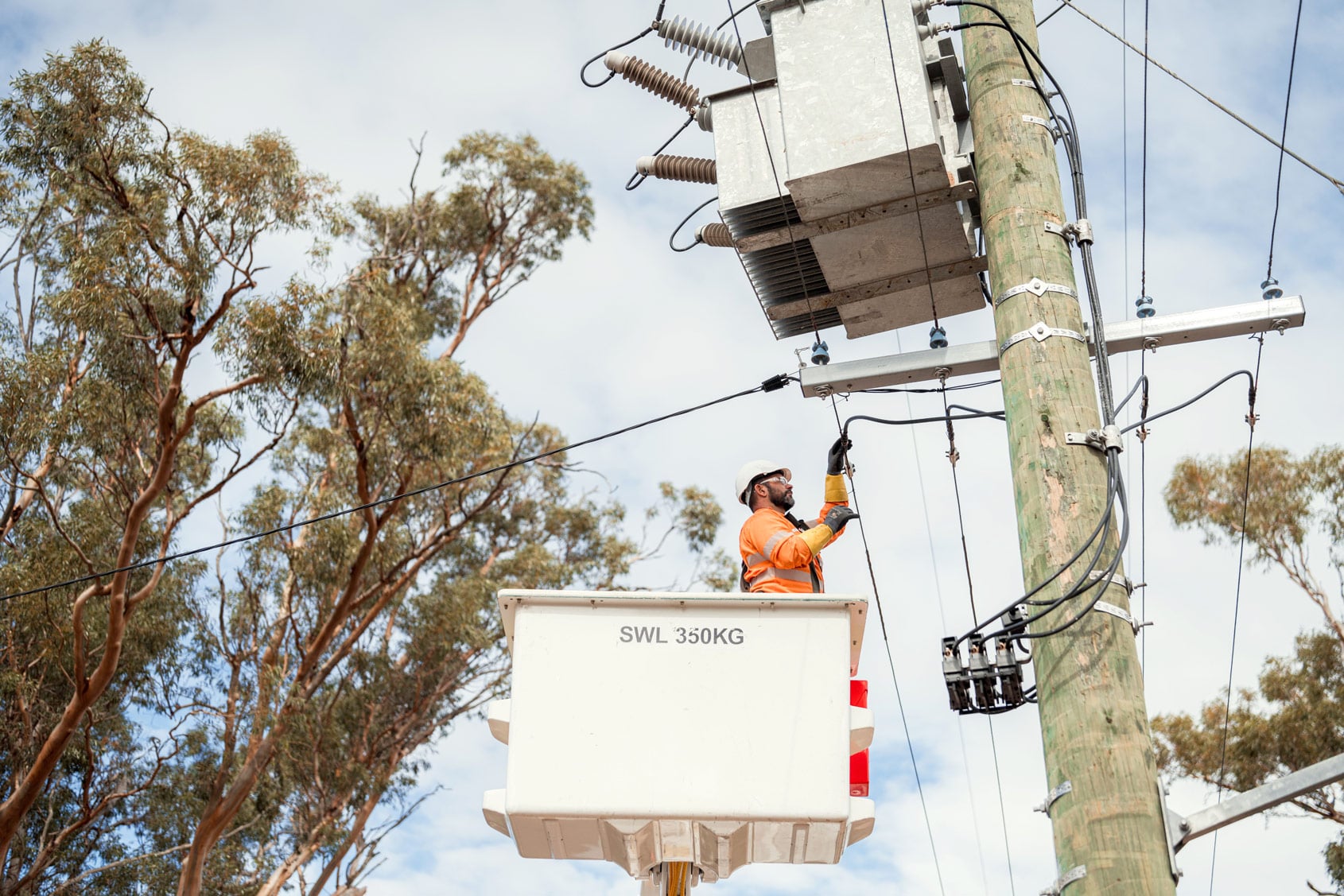 Utility worker in a elevated work platform servicing electrical equipment on a power pole.
