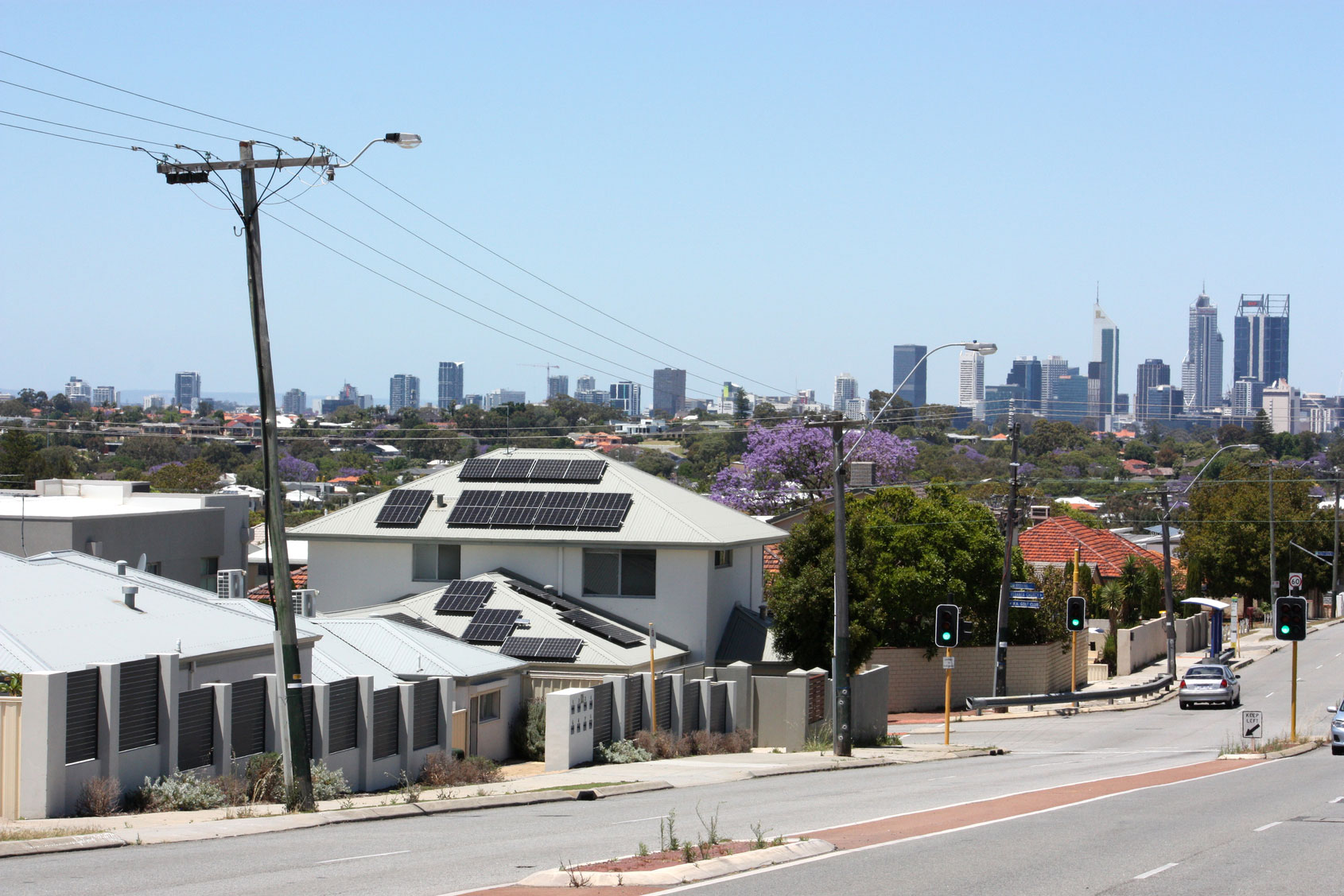 Electricity distribution lines running down a suburban street with Perth CBD skyline in the distance