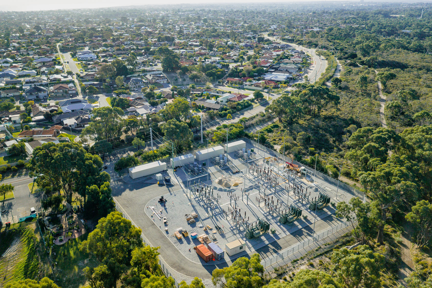 Aerial view of an electrical substation beside a suburban neighborhood and wooded area.