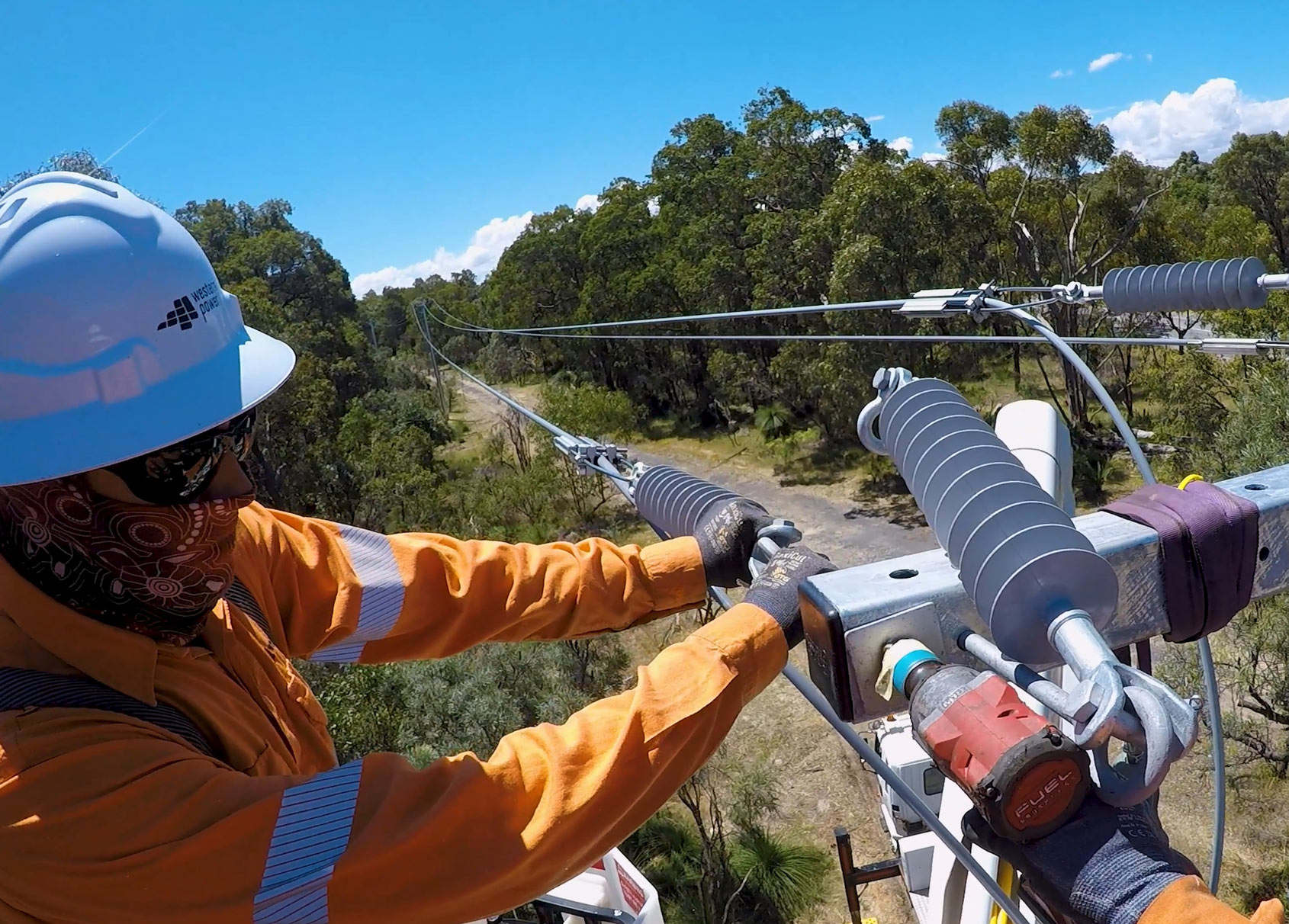 Two Western Power crew installing covered conductors from an elevated platform under a clear blue sky.