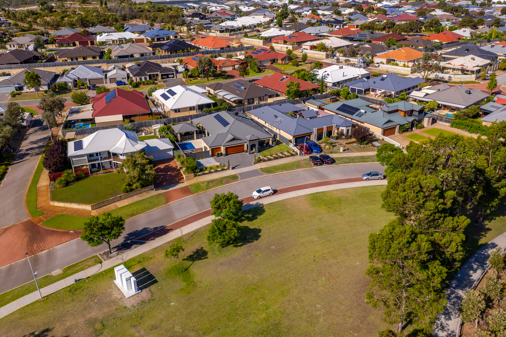 Aerial view of a suburban neighborhood in Ellenbrook with solar panels on rooftops and a community battery in a nearby park.