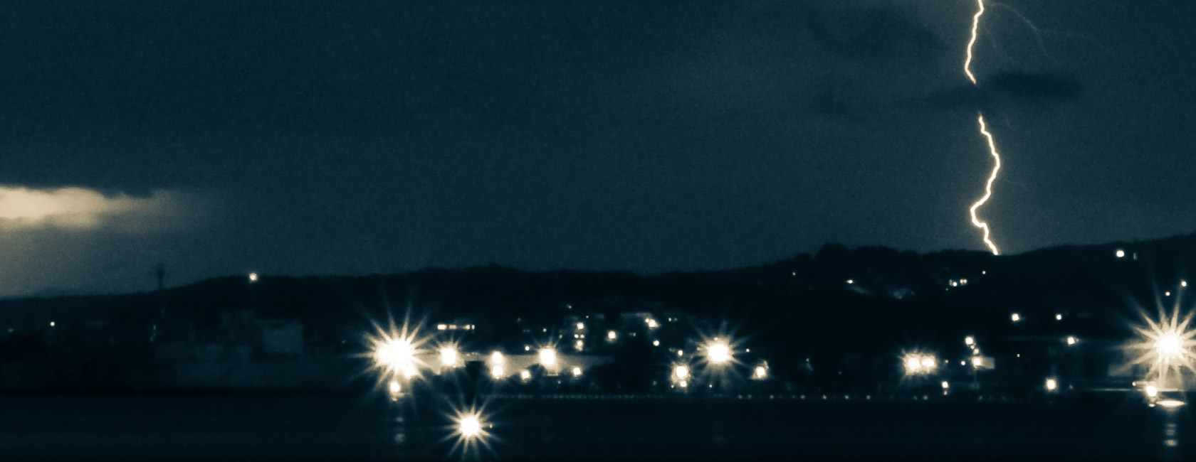 Lightning striking near a residential area at night with city lights glowing, highlighting the impact of storms on community power and safety.