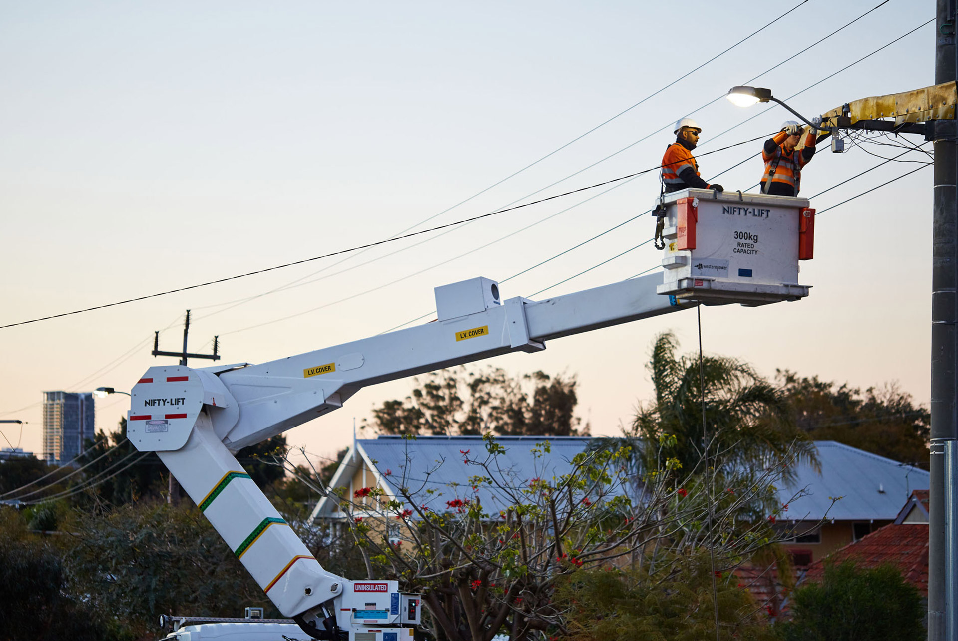 Western Power crew in a bucket lift repairing streetlights and power lines to restore electricity in a residential area.