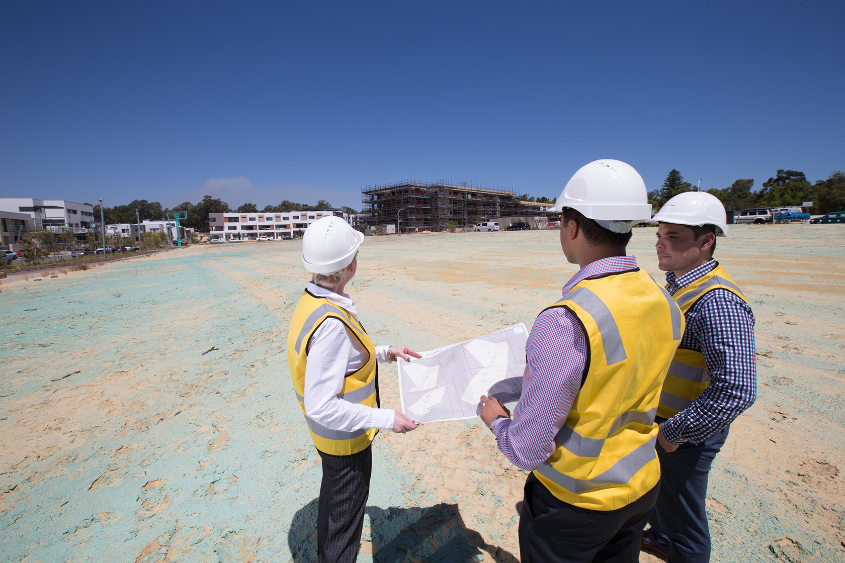 Three people in high-visibility clothing and construction hats looking at plans on a construction site.