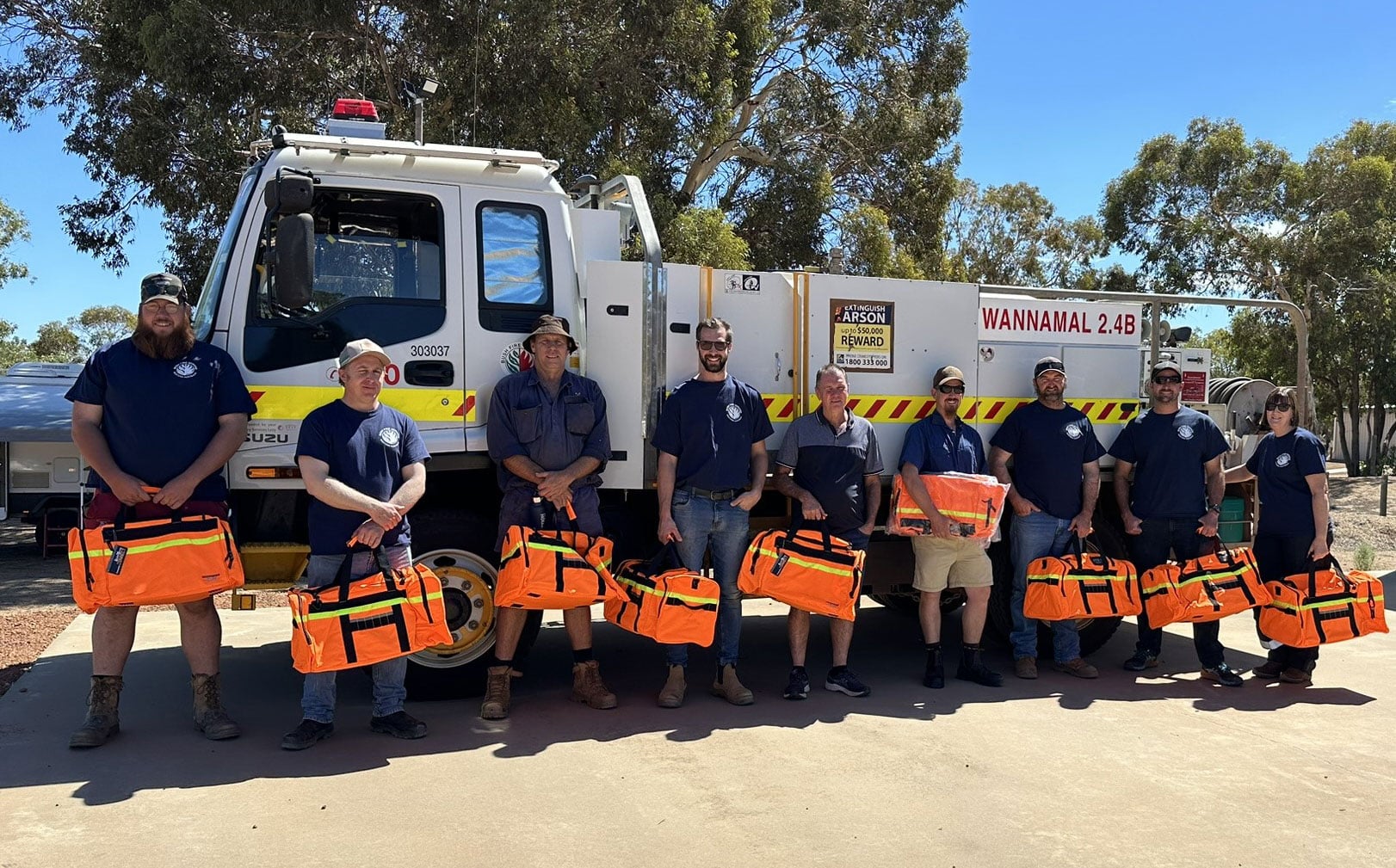 Wannamal Volunteer Bushfire Brigade members stand in front of a support truck holding orange emergency response bags.