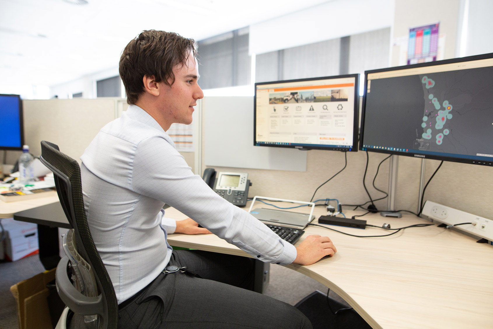 Man in office at desk working on dual monitors, one showing a website, the other a heatmap.