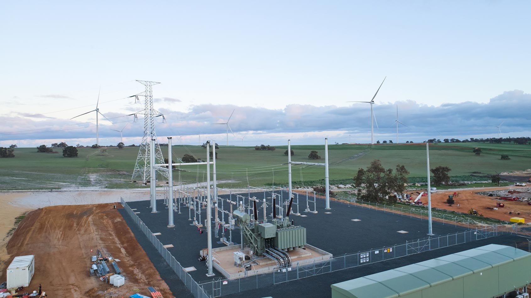 A substation in a rural area with wind turbines in the background.
