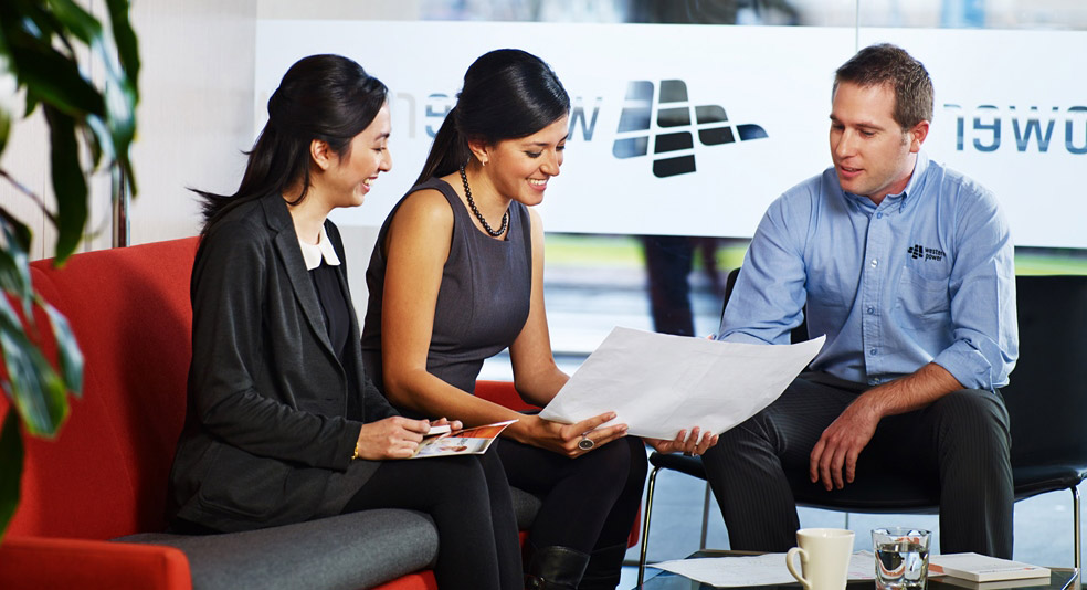 Three people in an office setting on lounges looking at a document.