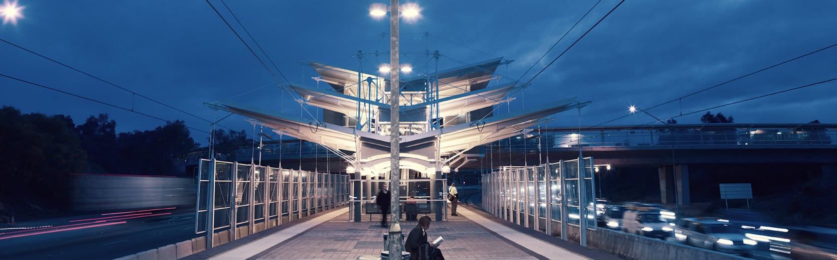 Modern train station at dusk with canopy lighting and nearby traffic.