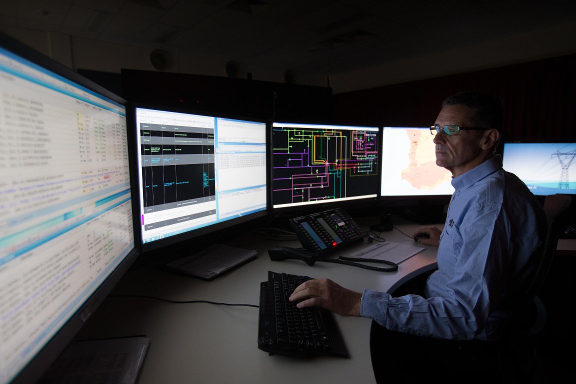 Man monitoring multiple computer screens in an electricity control center.