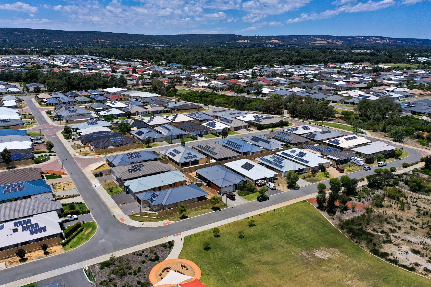 Aerial view of a suburban neighborhood with houses that have rooftop solar panels and a park in the foreground.
