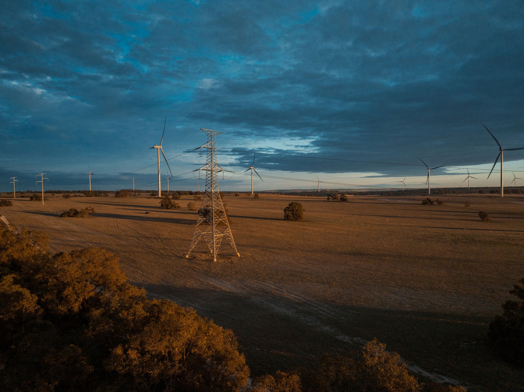 Transmission towers and wind turbines in a rural landscape at sunset, with power lines stretching across open fields.