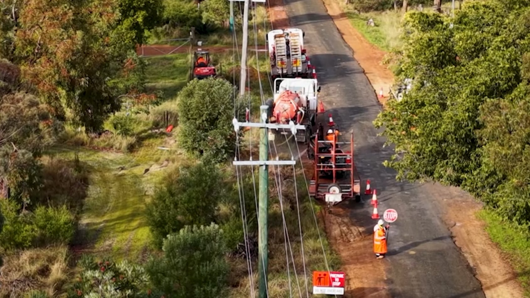 Western Power crews carrying out maintenance on a rural roadside power line, with work vehicles and traffic control in place.