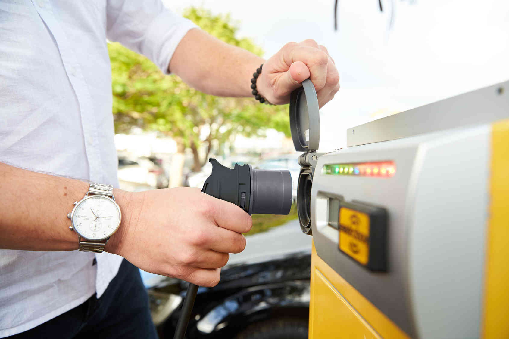 A person plugging a charging cable into an electric vehicle charging station outdoors.