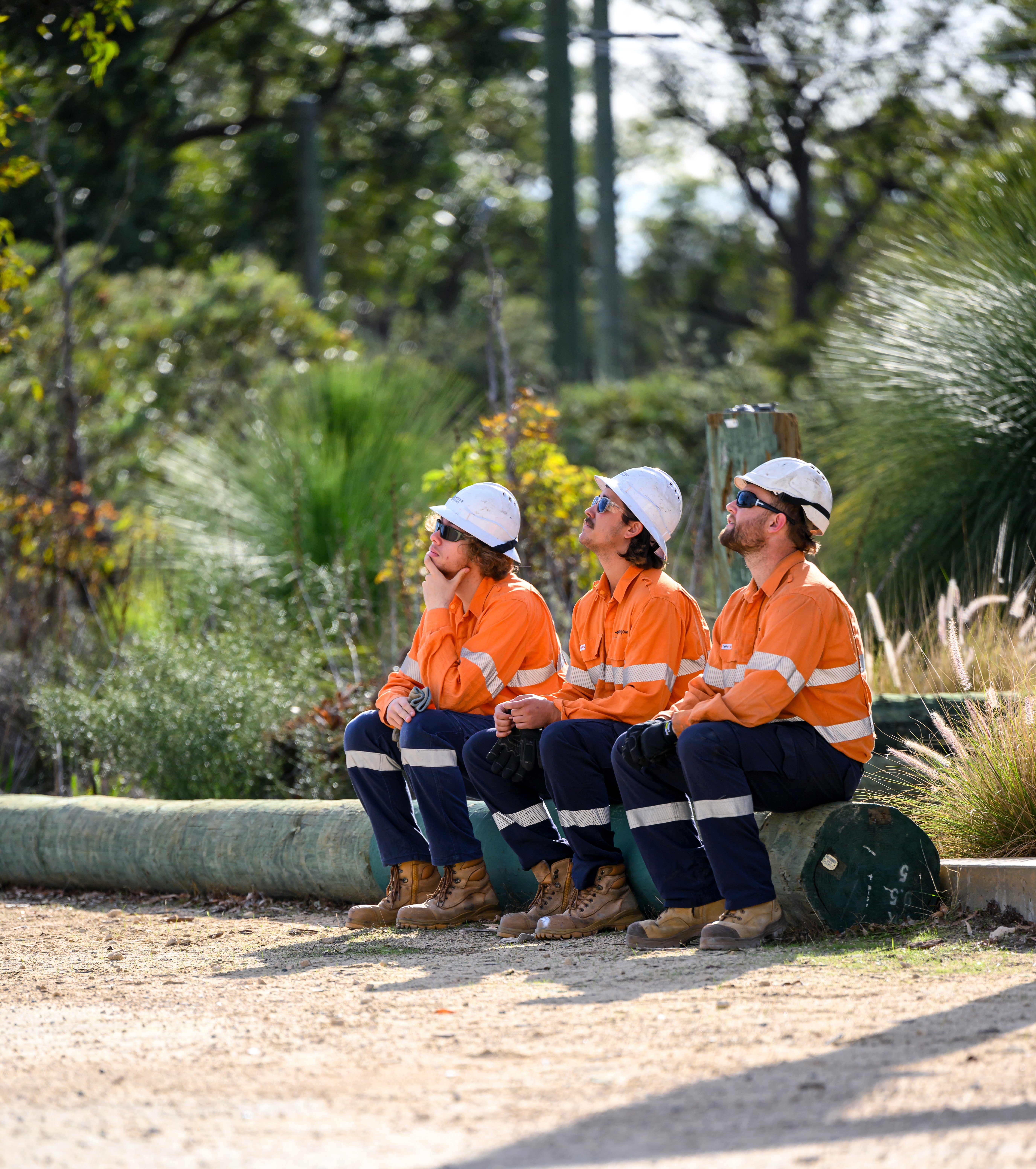 Western Power power employees sitting on a wall outside wearing PPE
