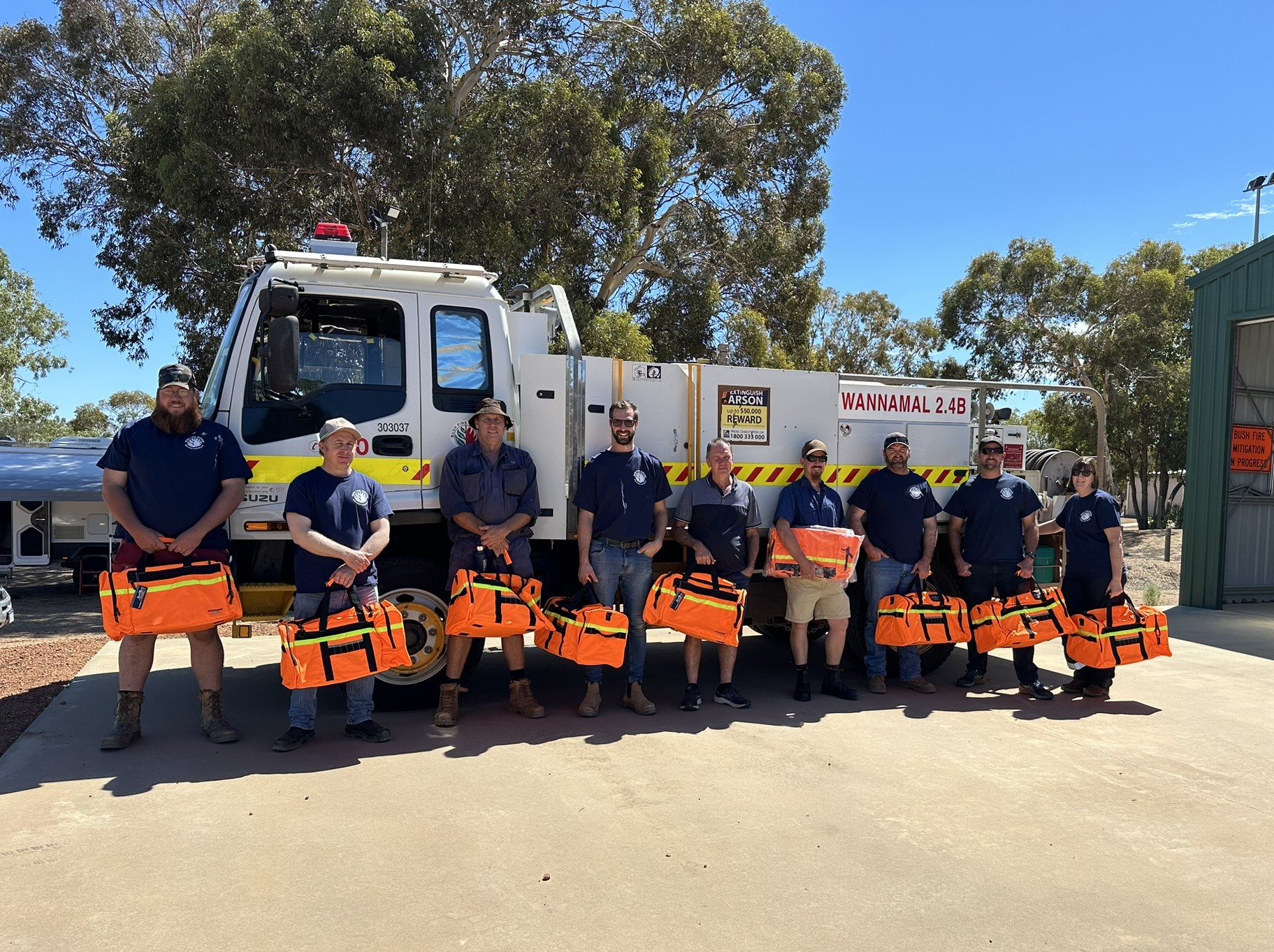 Wannamal Volunteer Bush Fire Brigade members standing in front of a fire truck holding bright orange emergency bags.