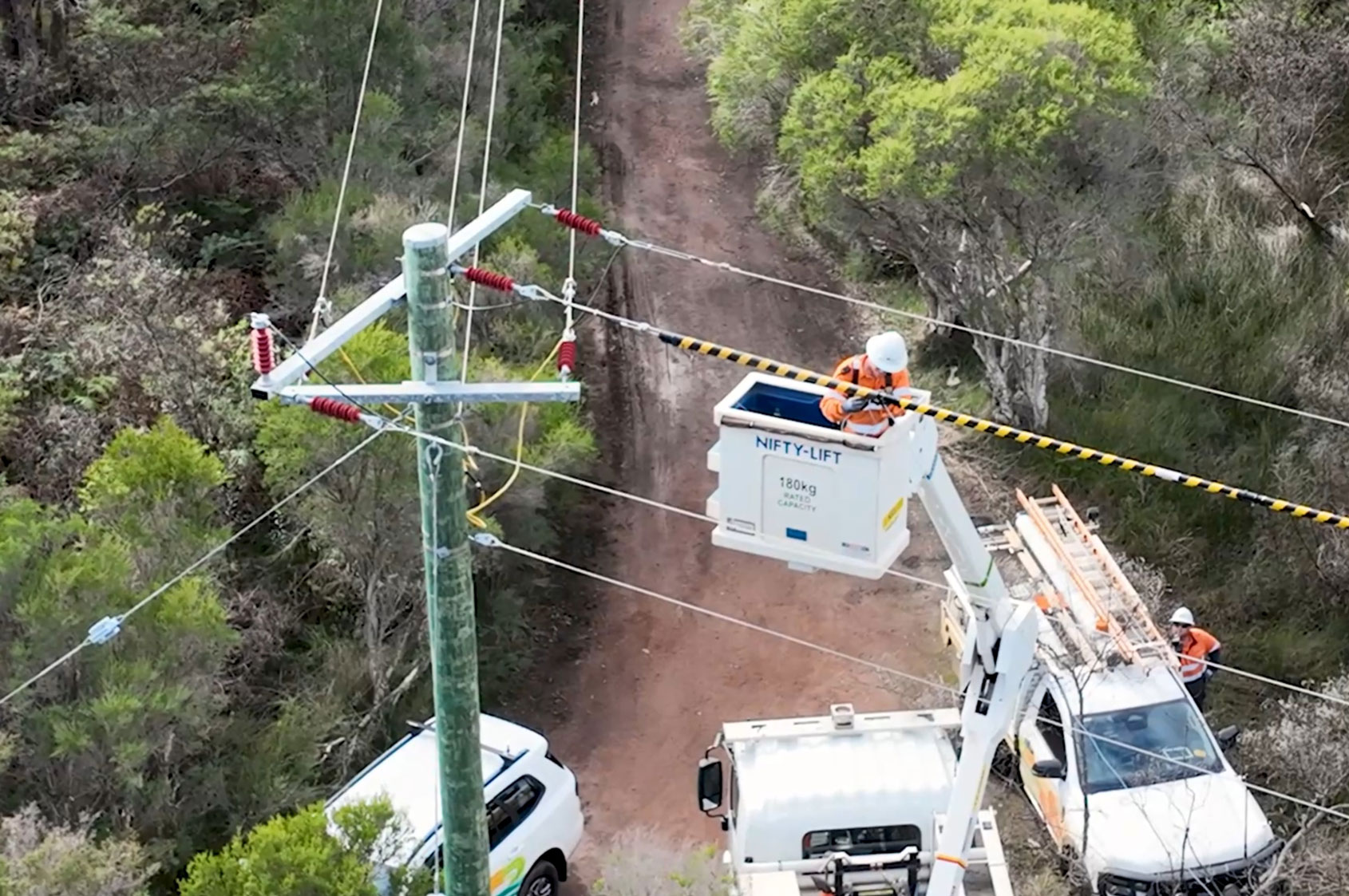 A Western Power crew member in a bucket lift installing a bird diverter on overhead power lines on a rural track.