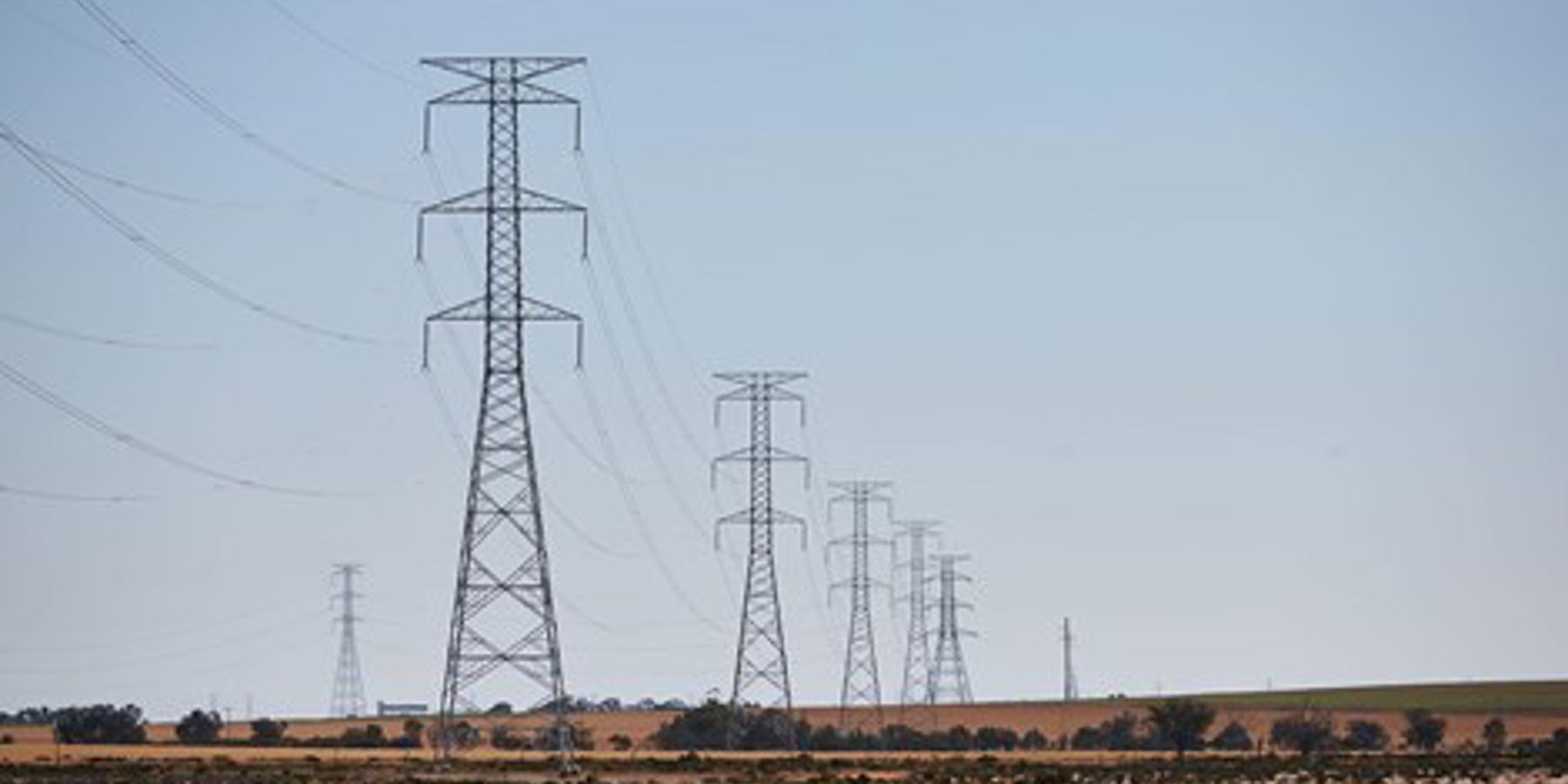 Fields with double circuit electricity transmission towers and lines in row continuing into the distance