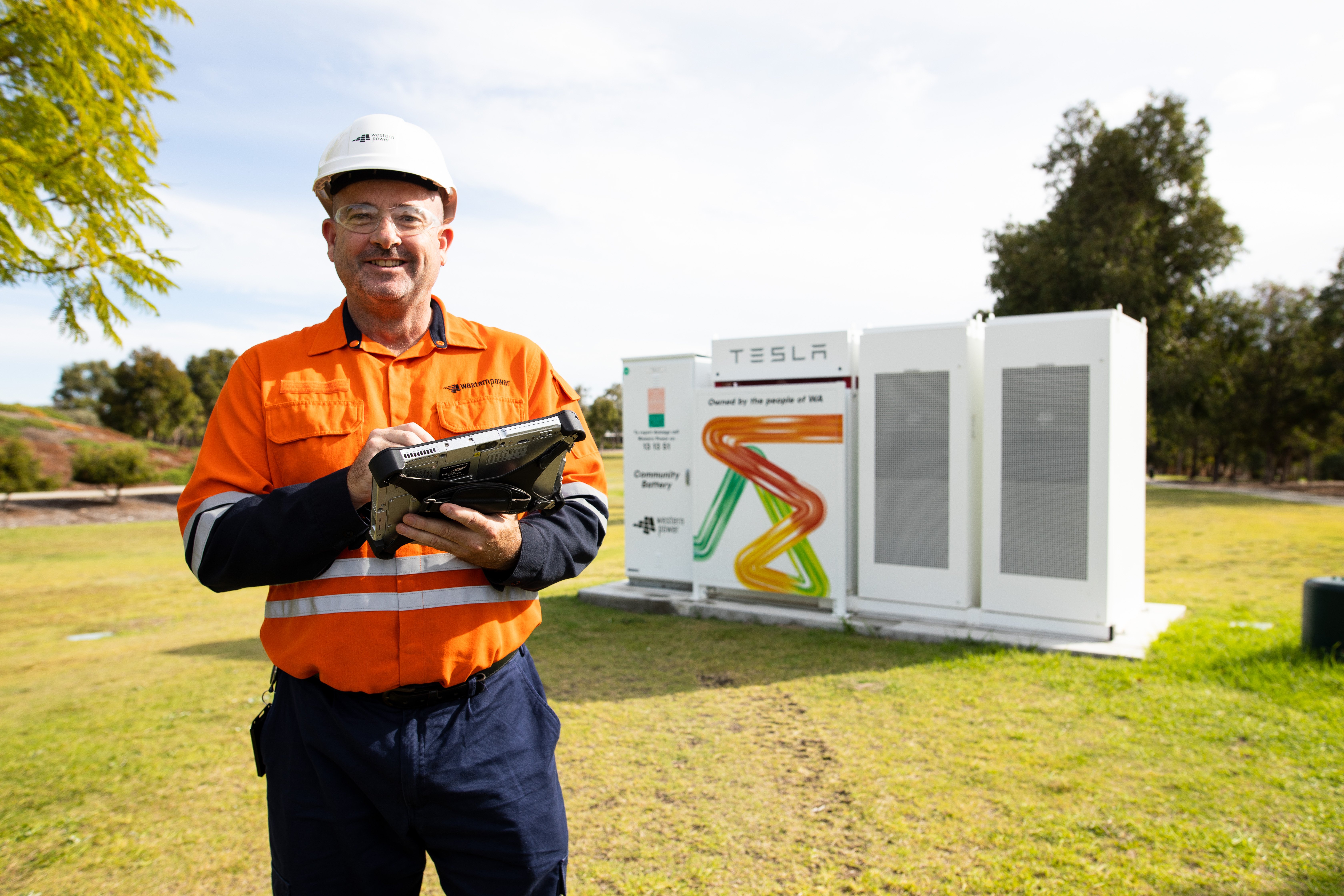 Western Power employee standing in a park in front of community battery.