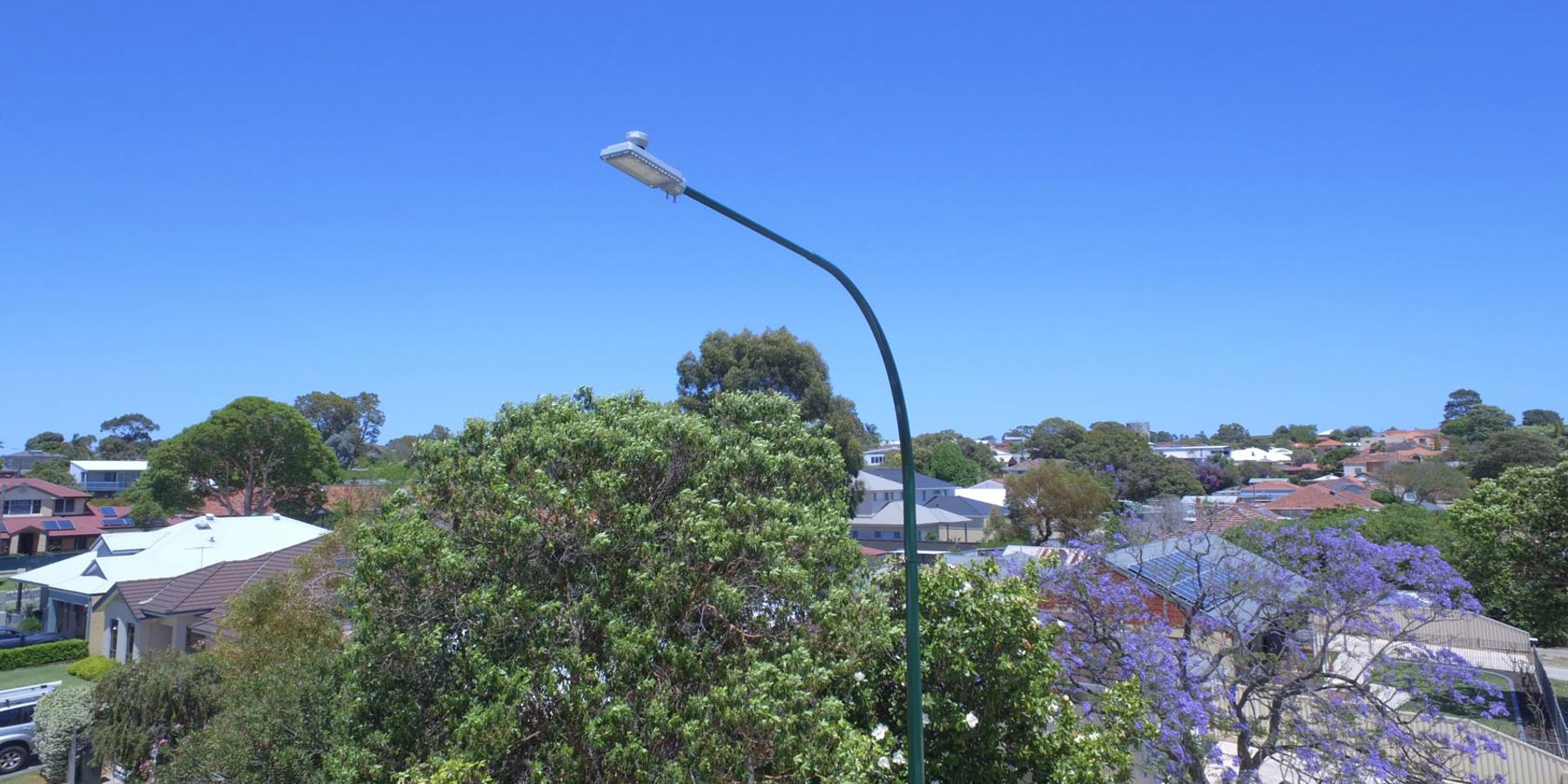 A streetlight in a residential suburb with trees in the background